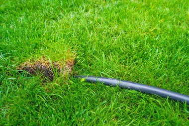 Kimyasalların ve çöplerin doğaya salınımı. Bilinmeyen bir kapasiteye sahip bir hortum yemyeşil çimenlere yönlendirilir. Yeşil çimlerden siyah bir plastik boru çıkıyor..