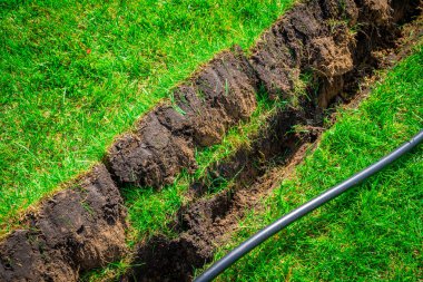 Plastik boru döşemek için çimlere kazılmış bir hendek. Yeraltı tesisatı için en üst çimen tabakasını kaldırdım.