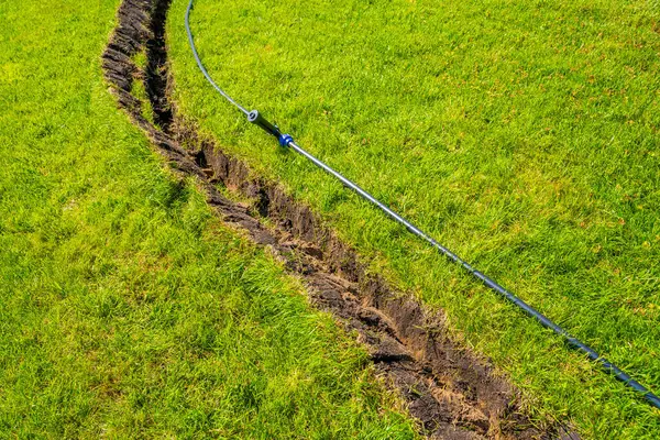 在草坪上挖的用来铺设管道和安装灌溉系统的沟渠 青草地和草根系统下的土壤 图库照片