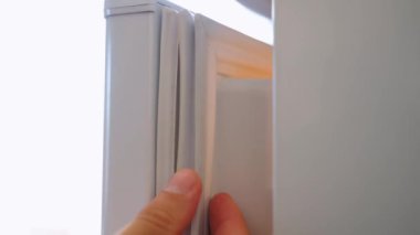 Çatlaklı, yıpranmış bir buzdolabı mührünün yakın çekimi. Bir el buzdolabının kapısında yırtık bir manyetik lastik bandı gösteriyor. Yüksek kalite 4k görüntü