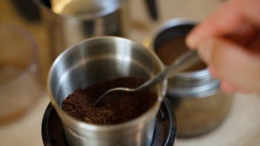Bir el taze öğütülmüş kahveyi çay kaşığının içine atar, gayzer kahve makinesinin arka planına yakın plan çekilir. Yüksek kalite 4k görüntü