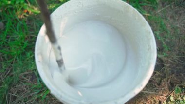 Ağaç boyasını bir kovanın üst görüntüsünde karıştırmak. Bahçede ağaç bakımı, mevsime hazırlık. Yüksek kaliteli FullHD görüntüler