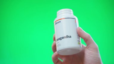 Kyiv, Ukrayna - 4 Ocak 2025: El, GymBeam 'den gelen bir kavanozdan yeşil arka planda avucunun içine Ashwagandha hapları döker. Yüksek kalite 4k görüntü