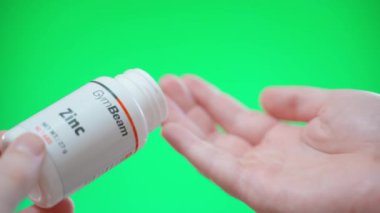 Kyiv, Ukrayna - 4 Ocak 2025: El, GymBeam 'den gelen çinko tabletleri yeşil arka plandaki avucuna döküyor. Yüksek kalite 4k görüntü