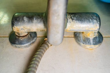 Banyo musluğu skalayla kaplı ve aşınma yakın plan, alt manzara. Tesisatta sert su ve maden yatakları..