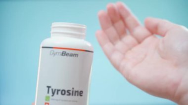 Kyiv, Ukrayna - 4 Ocak 2025: El, Jimnastik Beam 'den bir kavanoz Tyrosine tutar ve mavi bir arkaplana yakın plan el kapsülleri döker. Yüksek kalite 4k görüntü