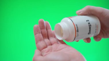 Kyiv, Ukrayna - 4 Ocak 2025: El jimnastik aletinden bir kutu Omega tutar ve yeşil arka planda avucunuzun içine kapsüller döker. Yüksek kalite 4k görüntü