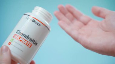 Kyiv, Ukrayna - 4 Ocak 2025: Elinizde GymBeam 'den bir kavanoz Chondroitin Sulphate bulunmakta ve mavi arka planda kapsülleri avucunuzun içine doldurmaktadır. Yüksek kalite 4k görüntü