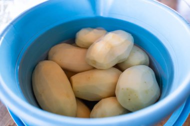 Mavi kovada soyulmuş patatesler ve yakın plan su..