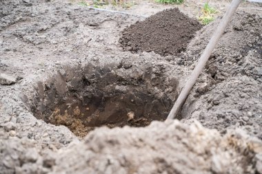 Toprağa kazılmış yuvarlak bir çukur ve içinde bir kürek..