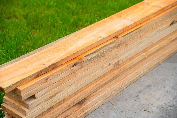 İnşaat için ahşap tahtalar yeşil çimlerin üzerine yığılmış, yakın plan..