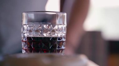 Arka planda bir adam kalkıyor ve uzaklaşıyor. Önde kristal bardakta güçlü bir alkollü içecek var. Yüksek kaliteli FullHD görüntüler
