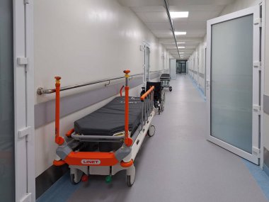 LVIV, UKRAINE - 25 Mart 2024: Hasta yatakları ve tek tekerlekli sandalyenin yer aldığı parlak ışıklı hastane koridoru.