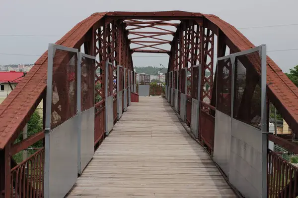 Empty red bridge with industrial design, cloudy sky.