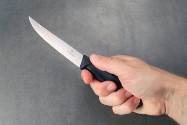 LVIV, UKRAINE - 25 Haziran 2024: Gri arkaplan üzerinde paslanmaz çelik bir bıçakla siyah saplı mutfak bıçağını tutan bir elin yakın çekimi.