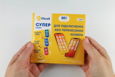 LVIV, UKRAINE - 25 Haziran 2024: Beyaz bir arkaplanda Ukrayna metin ve servis detaylarının yer aldığı sarı bir Lifecell SIM kart paketi tutan eller.