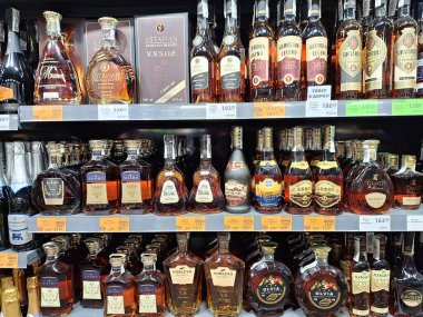 LVIV, UKRAINE - 10 Temmuz 2024: Görüntü bir süpermarket rafında çeşitli brendi şişelerini gösteriyor. Şişelerin çoğu kahverengi ve altın etiketli. Şişelerin fiyatları açıkça görülüyor..