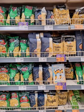 LVIV, UKRAINE - 30 Ağustos 2024: Birçok makarna türü süpermarket raflarında düzenli olarak düzenlenir, gün ortasında yerel bir markette çeşitli şekiller, boyutlar ve ambalajlar sergilenir.