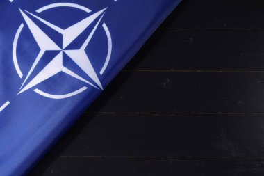 LVIV, UKRAINE - 03 Eylül 2024: Mavi ve beyaz NATO bayrağı, amblemini vurgulayan koyu ahşap bir yüzey üzerinde duruyor. Bu görsel, ittifakın üye ülkeler arasındaki karşılıklı savunma ve işbirliğine olan bağlılığını vurguluyor..