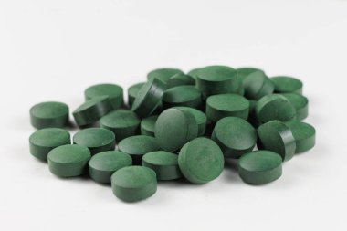 Küçük, yuvarlak yeşil tabletlerden oluşan bir koleksiyon beyaz bir yüzeye dağılmış, canlı renklerini ve sağlıklı beslenmek için potansiyel kullanımlarını vurgulamıştır..