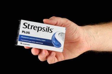 LVIV, UKRAINE - 13 Ocak 2025: Bir el siyah bir arkaplana karşı yatıştırıcı renkler ve açık etiketleme içeren, boğaz ağrısını dindirmek için bir ilaç kutusu sunar.