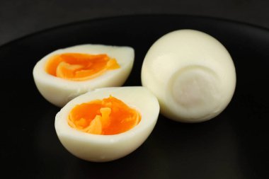 Yumuşak kaynamış yumurtalar siyah bir tabakta sunulur, kremsi sarıları ve pürüzsüz beyaz dış görünüşleri sergilenir..