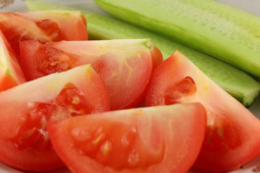 Sulu kırmızı domatesler ve çıtır çıtır salatalıklar beyaz bir tabakta ustalıkla düzenlenmiştir. Mutfak atmosferinde taze ve sağlıklı bir yemek seçeneği sunulmaktadır..