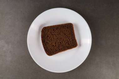 Siyah bir ekmek dilimi, düz beyaz bir tabağa, koyu bir yüzeye yerleştirilir, desen ve rengini gösterir..