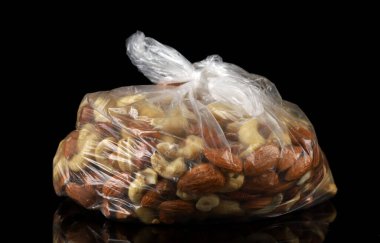 Şeffaf bir torba koyu bir fındık zeminine karşı çeşitli fındık tutar..