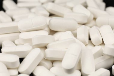 Farklı şekilleri gösteren çeşitli beyaz haplar karanlık bir yüzeye saçılmış..