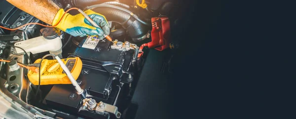 A technician checking DC voltage stable of the car battery with digital multimeter probe, panoramic banner with copy space on black background