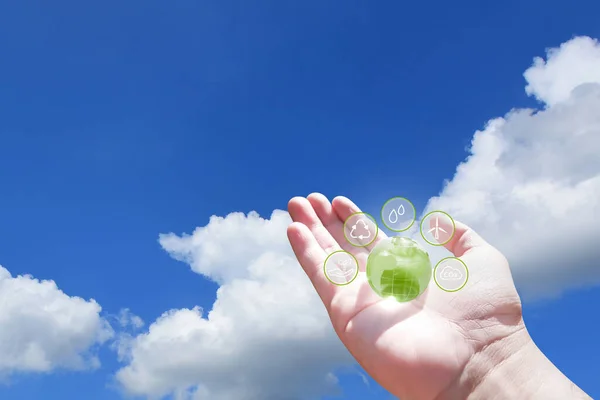 Hand holding green globe with eco energy icon on blue sky with white clouds background, Clean energy concept