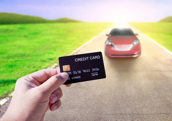 Hand holding credit card with car on the road blurred background. Online shopping and car rental concept
