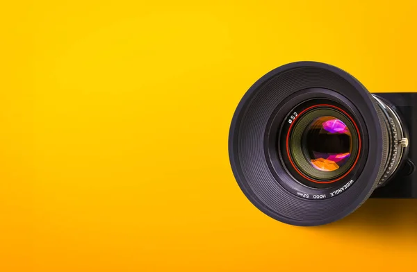 Front lens of vintage film camera with black body isolated on yellow or orange background with copy space.