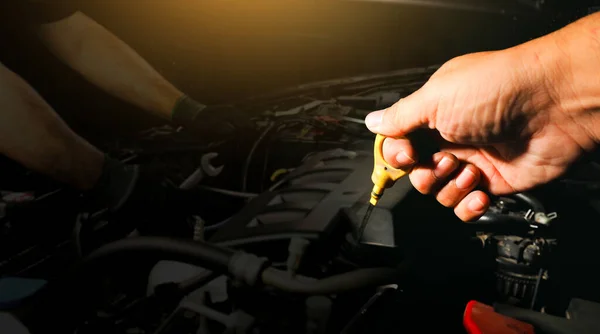 The mechanic is pulling the oil dipstick in the car engine compartment to check the motor oil level, Mechanic repairing a car on blurred background, double exposure, Car maintenance service concept.