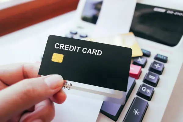 Hand holding credit card with printing calculator on table, black credit card mock in human hand, The concept of financial operations and credit card in the office.
