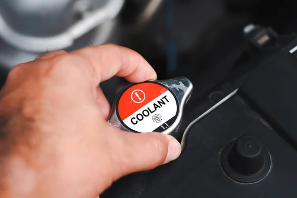 Close up a coolant cap of the car radiator cooling system. Mechanic hand opens car radiator cap to inspect and add coolant in a car engine compartment. Automotive parts concept