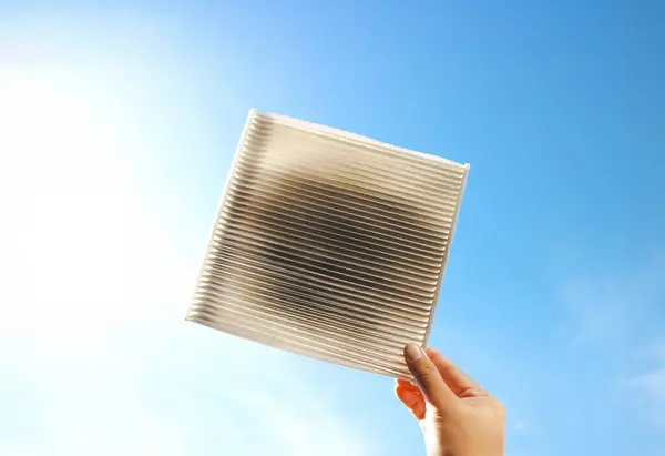 Car air conditioner filter clogged and dirty in a hand on blue sky background with sunlight , Car spare parts concept