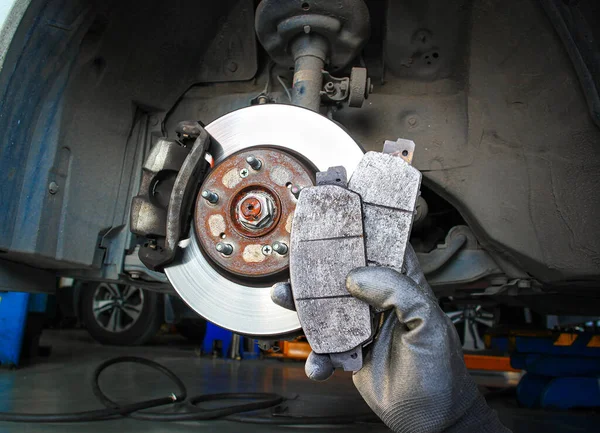 Used car brake pads in the hands of a mechanic with brake discs and brake calipers on the background , Car spare parts and maintenance concept