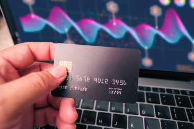 Bilgisayarda insan elinin tutulduğu kredi kartı veya banka kartı ve iş grafiği arka plan ve mali teknoloji kavramında bulanıklaştırıldı