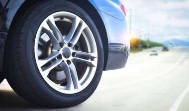 Gri lüks bir araba tekerleğine yakın, açık yolda park etmiş siyah lüks bir arabanın arka tarafına yakın, otomotiv konsepti.