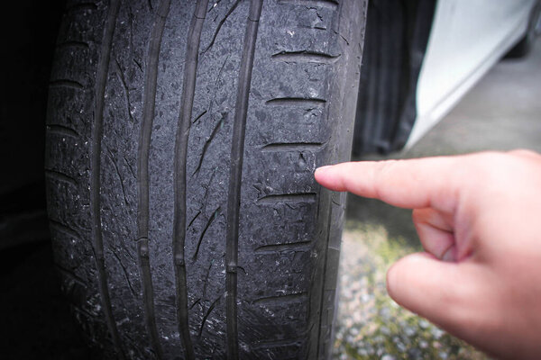 A hand pointing to worn out a car tire tread , Close up of car tire tread deterioration from use , Car maintenance concept
