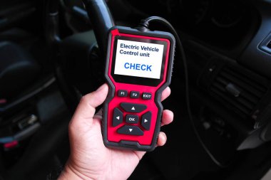 Elinizde elektrikli araç tanıları için OBD2 tarayıcı cihazı var. Elektrik Araç Kontrol Birimi Kontrolü gösteriliyor. Sistem testleri ve EV performans denemeleri için kullanılıyor.