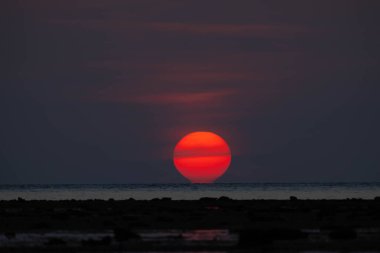 Gün batımında deniz ve sahil üzerinde sarı turuncu renkte parlak, büyük güneşin yakın çekim görüntüsü.