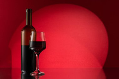 Glass and bottle of red wine on red background. Wine concept.