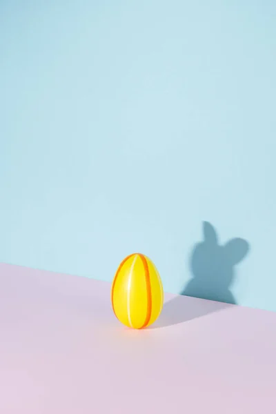 Easter egg with shadow in the shape of bunny or rabbit on pastel pink and blue background. Minimal Easter concept.
