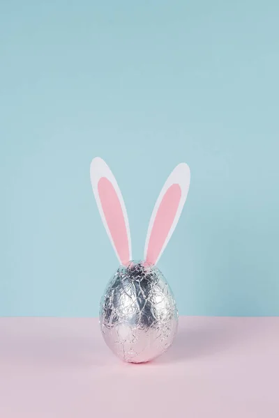 イースターエッグは ウサギやウサギの耳で銀箔に包まれています 最小限のパステルピンクと青 イースター休暇のコンセプト — ストック写真