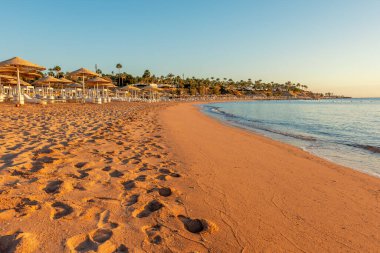 Günbatımında şemsiyeli tropik plaj manzarası. Tatil ve seyahat kavramı.