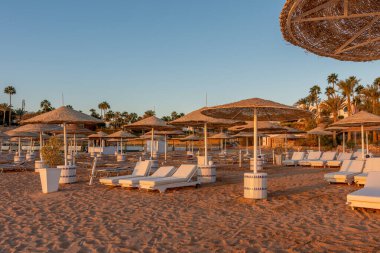 Günbatımında şemsiyeli tropik plaj manzarası. Tatil ve seyahat kavramı.