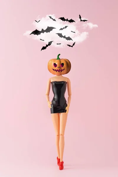 Girl doll with pumpkin head and bats on pink background. Creative Minimal Halloween party concept.